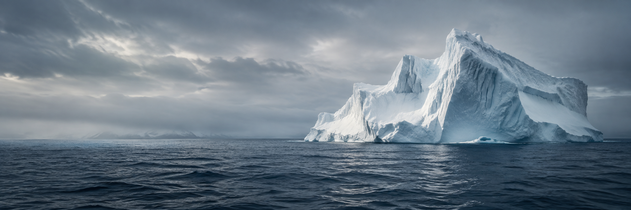 A blue-white iceberg standing above a wind-swept, dark sea